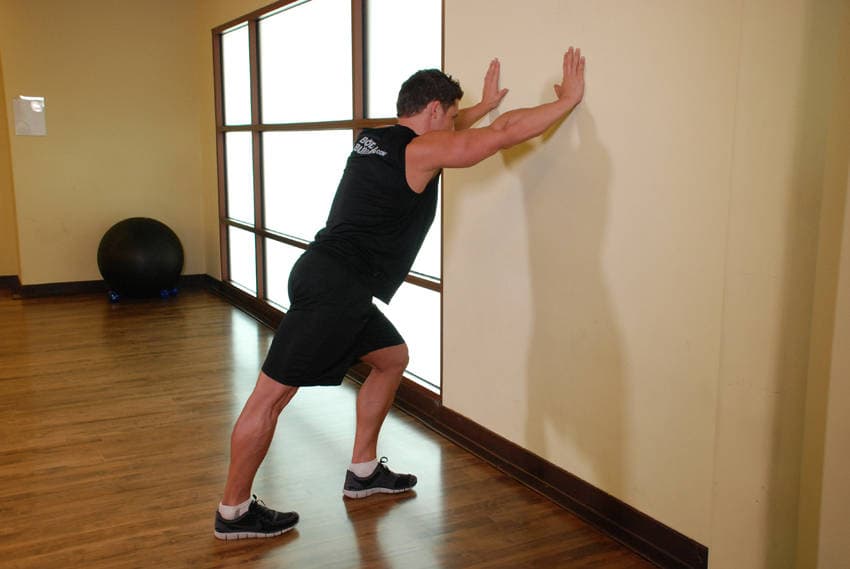 Estiramiento de gemelos con las manos en la pared, inicio